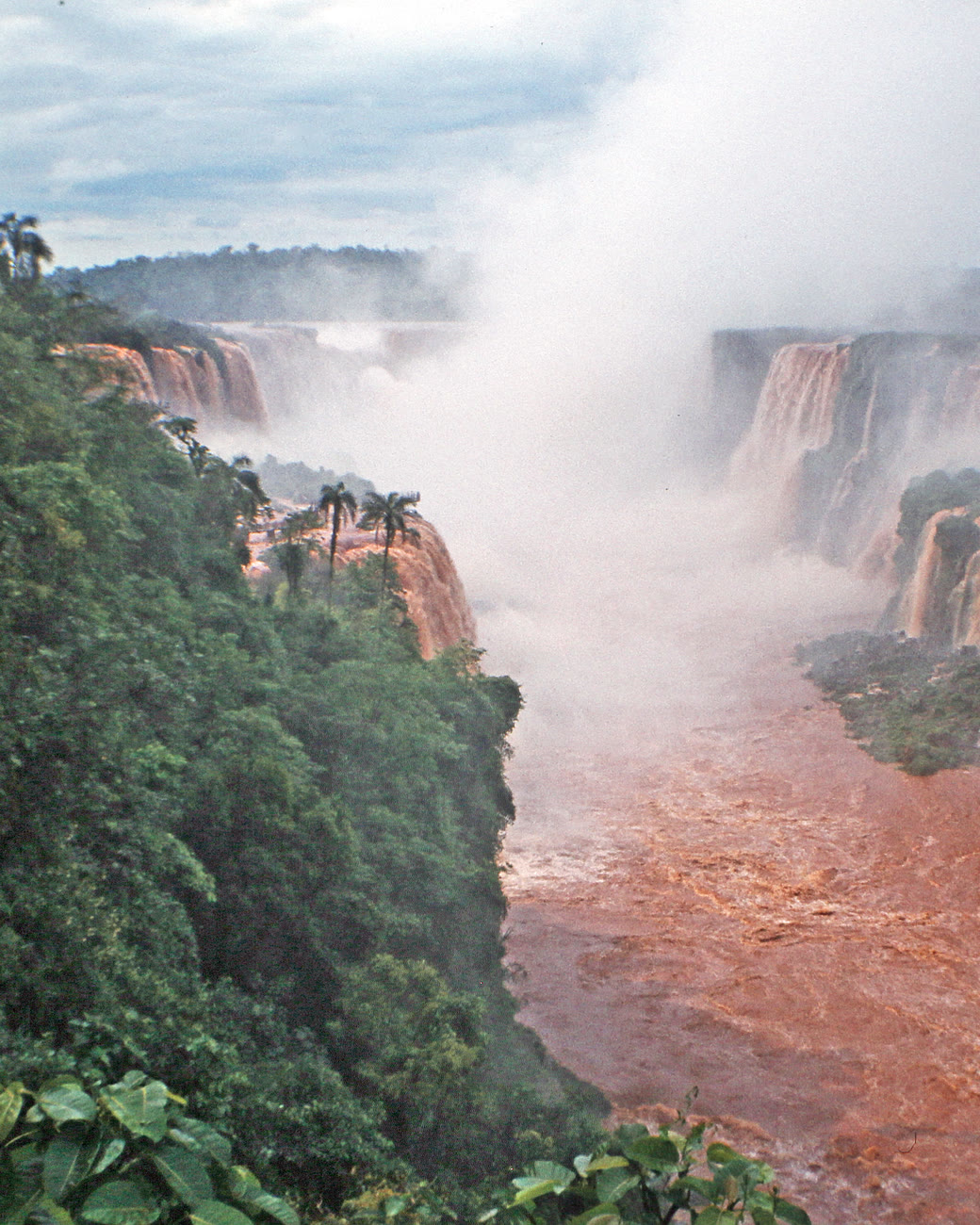 Quedas-d'água das Cataratas do Iguaçu caindo num cânion de rio avermelhado, entre a mata