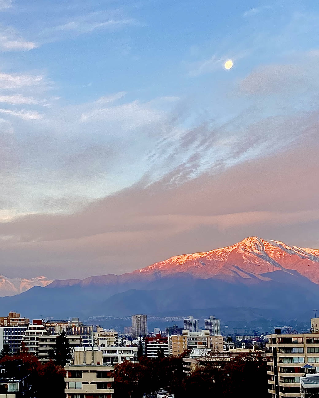 Cordilheira dos Andes com neve no alto, rosada pelo pôr do sol, atrás dos prédios de Santiago